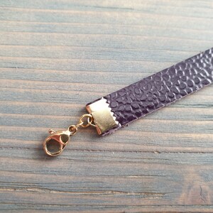May include: A close-up of a purple leather strap with a gold clasp. The strap is textured and has a subtle sheen.