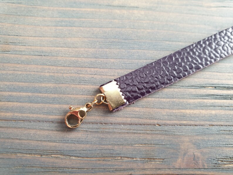 May include: A close-up of a purple leather strap with a gold clasp. The strap is textured and has a subtle sheen.