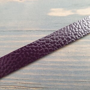 May include: A close-up of a dark purple leather strip with a textured surface. The strip is lying on a wooden surface.