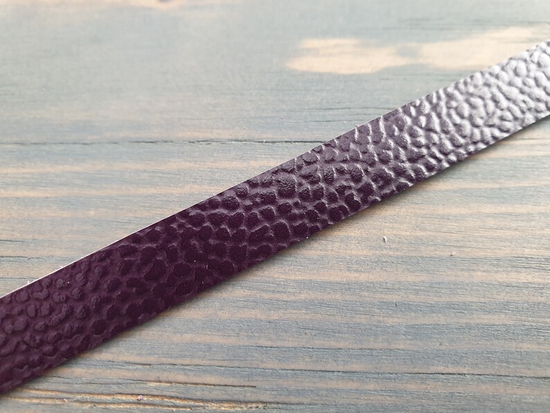 May include: A close-up of a dark purple leather strip with a textured surface. The strip is lying on a wooden surface.