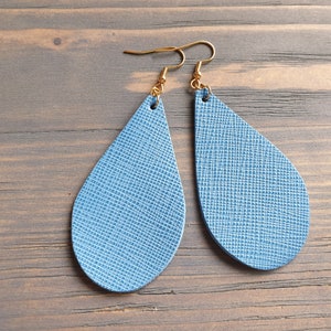 May include: A pair of teardrop-shaped earrings made of blue leather with a textured surface. The earrings have gold hooks.