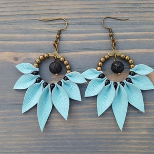 May include: A pair of dangle earrings with a light blue leather flower design, black beads, and a black lava rock bead in the center of each earring.