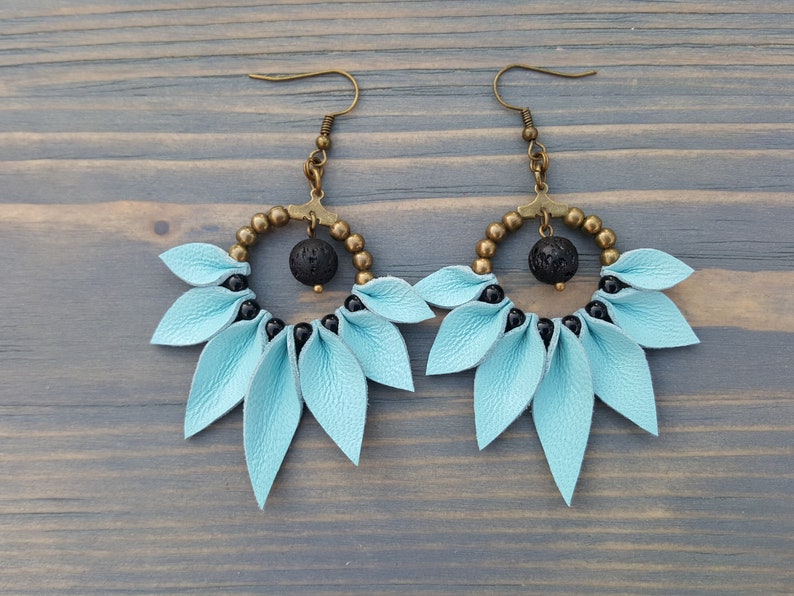 May include: A pair of dangle earrings with a light blue leather flower design, black beads, and a black lava rock bead in the center of each earring.