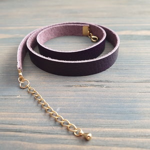 May include: A purple leather choker necklace with a gold chain extender. The choker is rolled and has a smooth, textured surface.