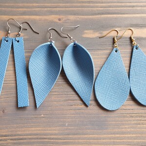 May include: Three pairs of blue leather earrings. The first pair is a long, rectangular shape. The second pair is a teardrop shape with a pointed end. The third pair is a teardrop shape with a rounded end.