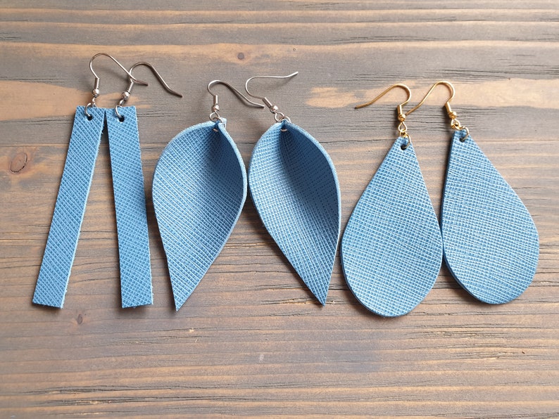 May include: Three pairs of blue leather earrings. The first pair is a long, rectangular shape. The second pair is a teardrop shape with a pointed end. The third pair is a teardrop shape with a rounded end.