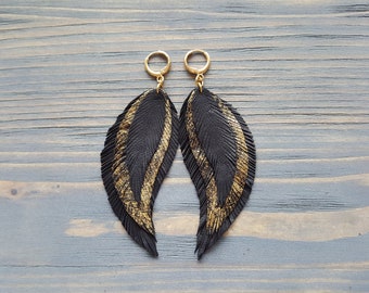 May include: A pair of black leather feather earrings with gold accents. The earrings are dangle style and have a gold hoop.