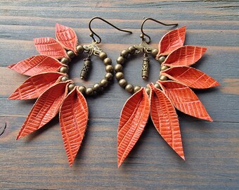 May include: A pair of orange leather earrings with a circle of brass beads and a small charm hanging from each earring.