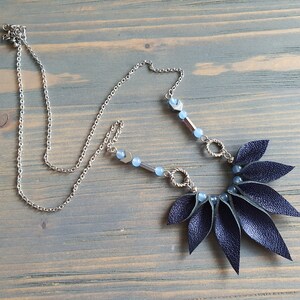 May include: A dark blue leather necklace with a silver chain and blue beads. The leather is cut into a fan shape with pointed ends.