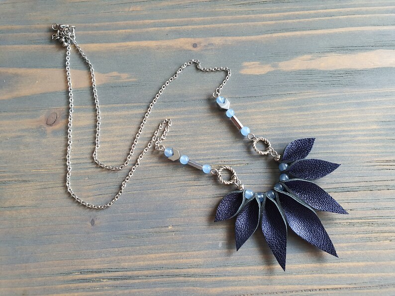 May include: A dark blue leather necklace with a silver chain and blue beads. The leather is cut into a fan shape with pointed ends.