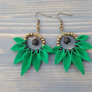 May include: A pair of green and black earrings with a round, beaded design and a black lava rock bead. The earrings have a leaf-like shape.