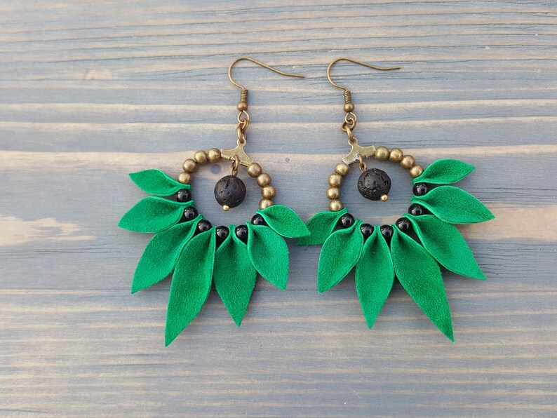 May include: A pair of green and black earrings with a round, beaded design and a black lava rock bead. The earrings have a leaf-like shape.