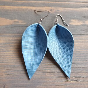 May include: A pair of blue leather earrings shaped like teardrops. The earrings have a textured surface and silver hooks.