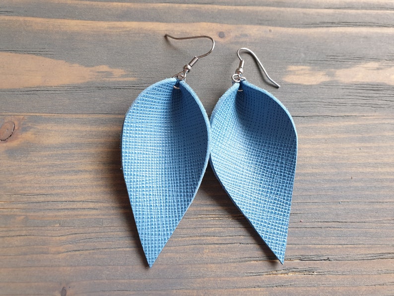 May include: A pair of blue leather earrings shaped like teardrops. The earrings have a textured surface and silver hooks.