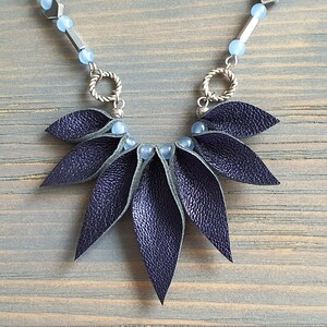 May include: A dark blue leather necklace with a geometric design. The necklace features a cluster of leather leaves and blue beads.