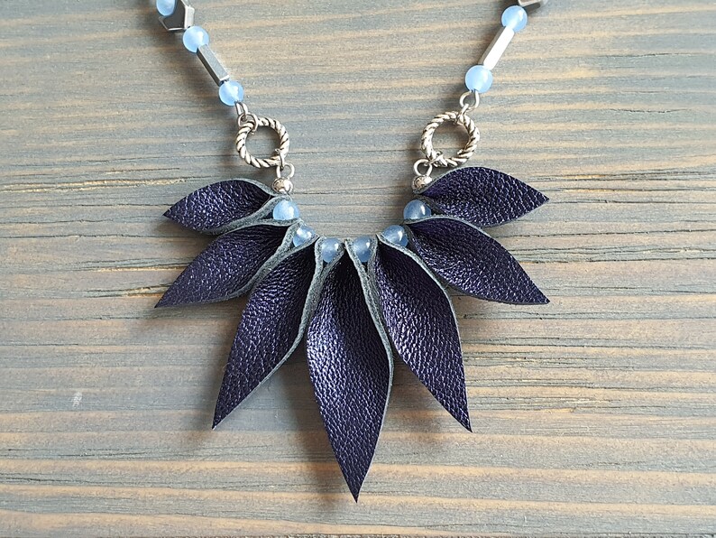May include: A dark blue leather necklace with a geometric design. The necklace features a cluster of leather leaves and blue beads.