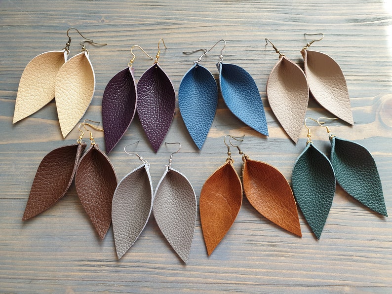 May include: A collection of leaf-shaped earrings in various colors, including beige, purple, blue, tan, brown, gray, orange, and green. Each pair features a textured surface and is suspended from a metal hook.