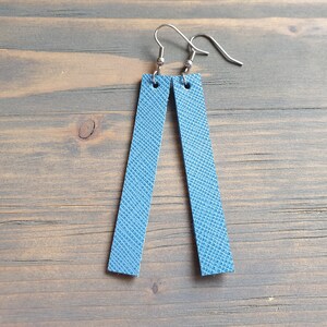 May include: A pair of blue leather earrings with silver hooks. The earrings are rectangular in shape and have a textured surface.