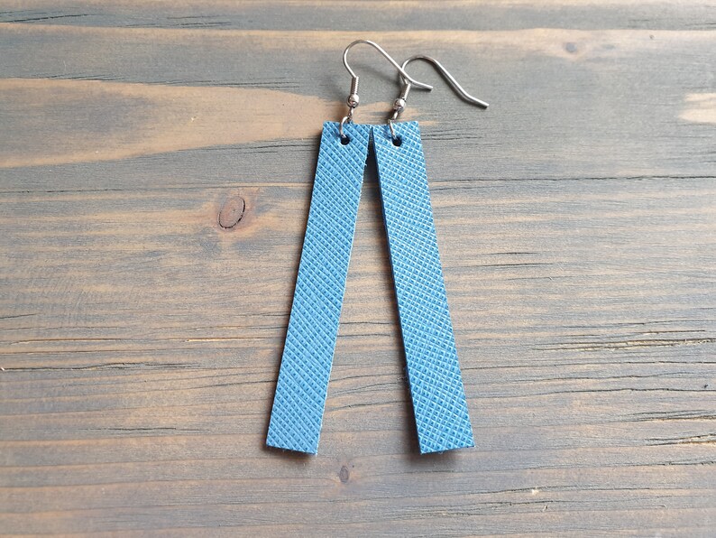 May include: A pair of blue leather earrings with silver hooks. The earrings are rectangular in shape and have a textured surface.