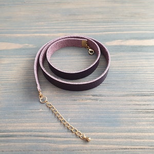 May include: A dark purple leather choker necklace with a gold clasp and extender chain.