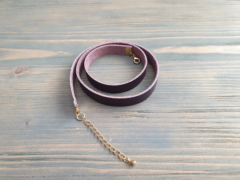 May include: A dark purple leather choker necklace with a gold clasp and extender chain.
