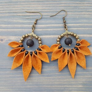 May include: A pair of dangle earrings with a gold-toned metal hoop and a cluster of orange suede leaves. The hoop is adorned with black beads and a black lava rock bead.