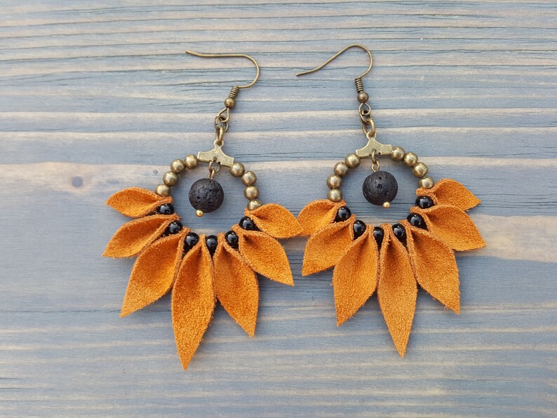 May include: A pair of dangle earrings with a gold-toned metal hoop and a cluster of orange suede leaves. The hoop is adorned with black beads and a black lava rock bead.