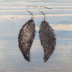 K&ouml;nnte beinhalten: Ein Paar silberne Federn-Ohrringe mit einem glitzernden schwarzen Finish.