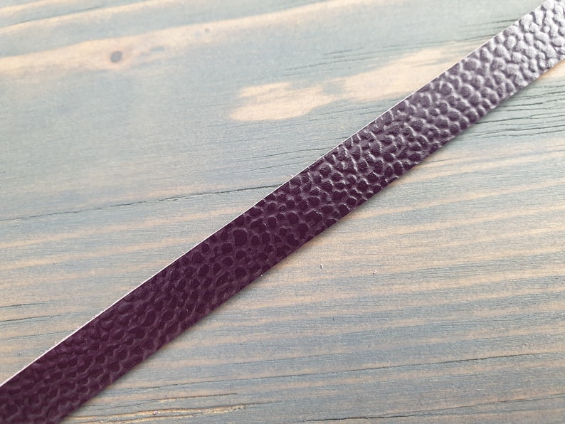 May include: A close-up of a dark purple leather strip with a textured surface.