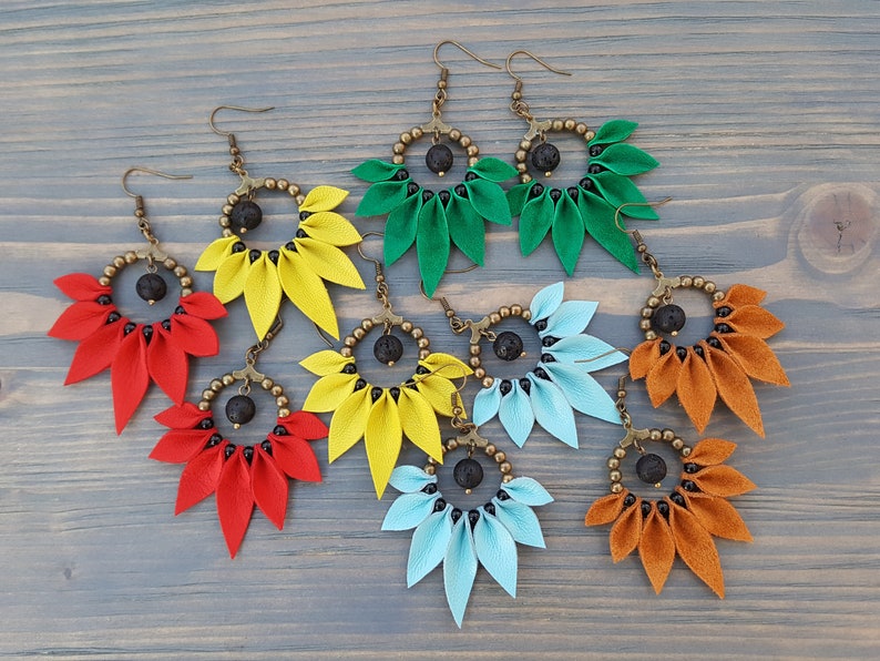 May include: Six pairs of earrings with a flower-shaped design. Each pair features a different color: green, yellow, red, blue, and orange. The earrings are made with leather and have a black lava rock bead in the center.