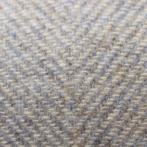 May include: Close-up of a woven fabric with a herringbone pattern. The fabric is a light gray color with a subtle blue hue.