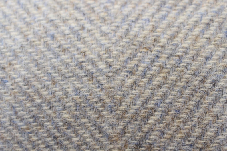 May include: Close-up of a woven fabric with a herringbone pattern. The fabric is a light gray color with a subtle blue hue.