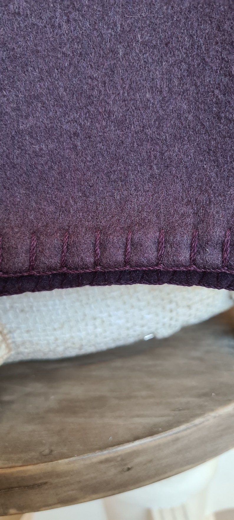 Op de afbeelding: Close-up van een donkerpaarse stof met een gestikte rand. De stof is zacht en pluche, en de stiksels zijn in een donkerdere tint paars.