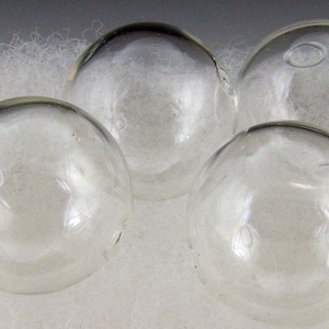 May include: Four clear glass spheres, each with a slightly different shape and size, are arranged on a white fuzzy surface.