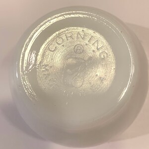 K&ouml;nnte beinhalten: Wei&szlig;e Corning Ware Sch&uuml;ssel mit einem runden Logo auf der Unterseite, das "Corning Ware USA" lautet.