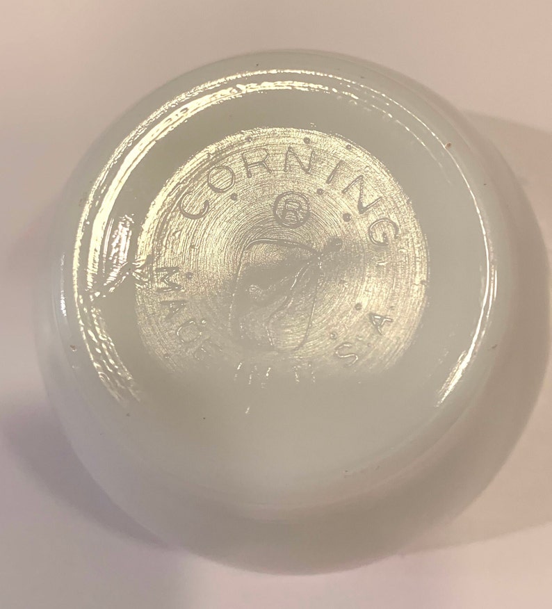 K&ouml;nnte beinhalten: Wei&szlig;e Corning Ware Sch&uuml;ssel mit einem runden Logo auf der Unterseite, das "Corning Ware USA" lautet.