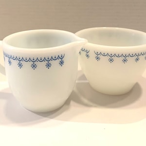 K&ouml;nnte beinhalten: Ein wei&szlig;es Milchk&auml;nnchen und eine Zuckerdose aus Milchglas mit einem blauen Schneeflockenmuster. Das Set hat einen Vintage-Look.