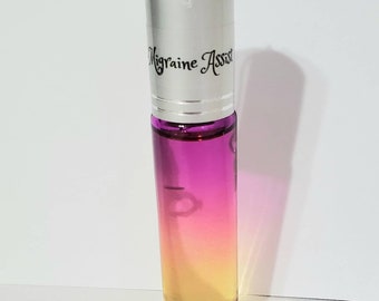 May include: A clear glass roll-on bottle with a gradient of colors, transitioning from yellow to pink. The bottle has a silver cap with the words "Migraine Assist" in black script. A black string is attached to the top.