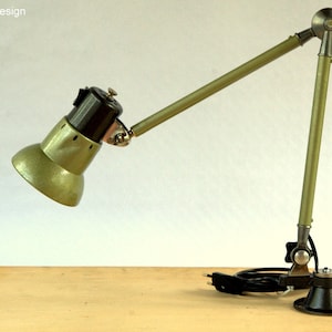 May include: A green metal desk lamp with a flexible arm and a clamp base. The lamp has a green metal shade and a black switch.