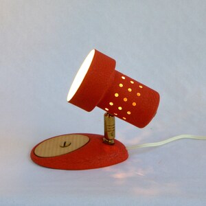 May include: A red and white desk lamp with a perforated shade. The lamp has a round base and a flexible arm.