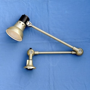 May include: A gold-coloured adjustable desk lamp with a white shade and a black base. The lamp has two arms that can be adjusted to different positions.