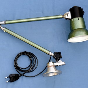 May include: A green and silver adjustable desk lamp with a black knob and a black electrical cord. The lamp has a white interior and a green exterior.