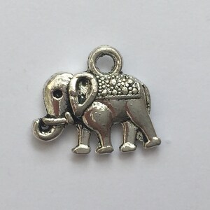 May include: A small, silver-colored elephant charm with a loop at the top for attaching to jewelry or other crafts. The elephant has detailed features, including a textured saddle and trunk. The charm is made of metal and has a vintage or antique appearance.