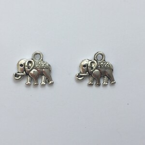 May include: Two small, silver-colored elephant charms. Each charm features a detailed elephant design with a textured back and a loop at the top for attaching to jewelry or other crafts. The charms are displayed against a white background.