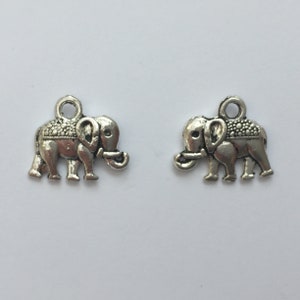 May include: Two silver-colored elephant charms. Each charm features an elephant with detailed trunk, ears, and a textured blanket design on its back. The charms have a small loop at the top for attaching to jewelry or other crafts.