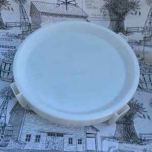 May include: White plastic round lid with four tabs on the side. The lid is on a white and black patterned surface.
