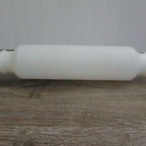 May include: A white rolling pin with a cylindrical body and rounded ends. The ends have a ridged design for grip. This kitchen tool is designed for rolling out dough for baking.