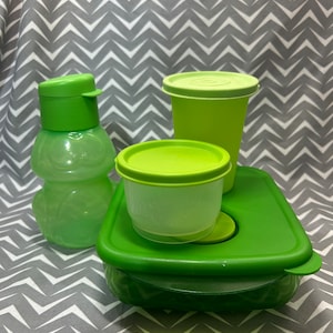 May include: A set of four green plastic containers with lids. The containers are different sizes and shapes. The largest container is a square shape with a lid that has a small green handle. The second largest container is a round shape with a lid that has a small green handle. The third largest container is a round shape with a lid that has a small green handle. The smallest container is a bottle shape with a lid that has a small green handle.