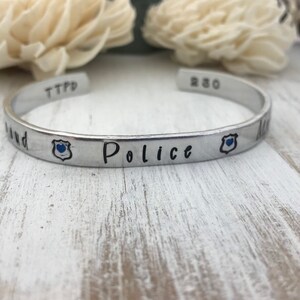 May include: A silver bracelet with the words "Police" and "TTPD" engraved on it. The bracelet also has two small blue badges with a heart in the center.