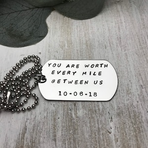 May include: Silver dog tag necklace with the text "You are worth every mile between us 10-06-18" engraved on it.